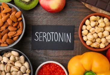 A black card with the word "SEROTONIN" written in chalk, surrounded by healthy foods like nuts, fruits, and vegetables.